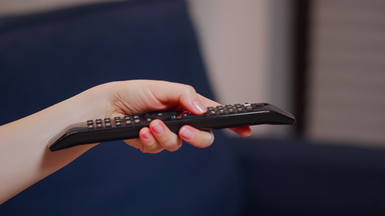 Close up of caucasian hand with TV remote switching channels